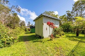 A small, single-story building with a sloped roof, surrounded by lush greenery and trees.