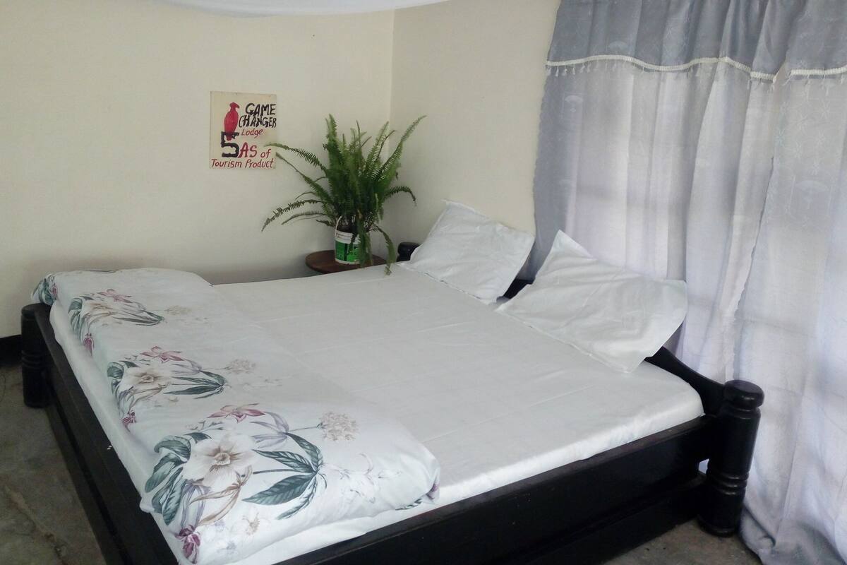A bed with floral bedding, a nightstand with a plant, and a sign indicating a game changer lodge.