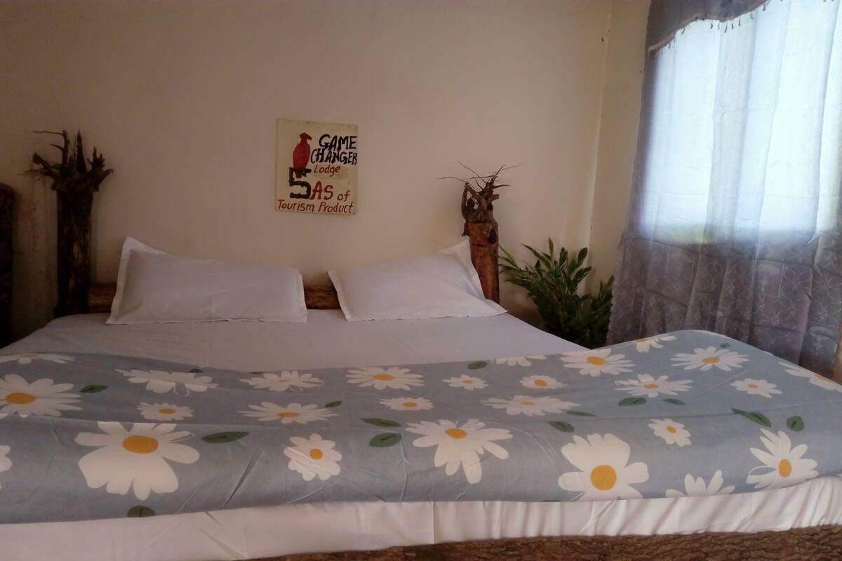 A bed with a floral bedspread, two white pillows, and a sign on the wall advertising a game changer lodge.
