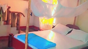 Una habitación con cama, ventana con cortinas, pared con un cuadro y suelo estampado.