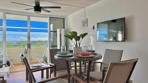 A dining area with a table, chairs, a ceiling fan, a TV, and a view of the outdoors.