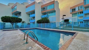 A swimming pool with a blue fence, surrounded by multi-story buildings with balconies.