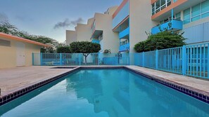 A swimming pool with a blue fence, surrounded by buildings with balconies and windows.