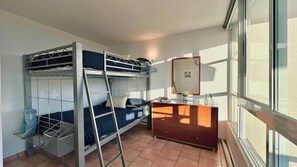 A dormitory room with bunk beds, a desk, and a window.