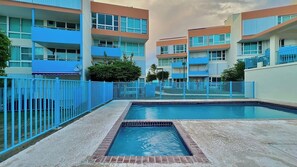 A swimming pool area with a blue fence, surrounded by multi-story buildings with balconies.