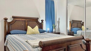 A bed with a wooden headboard, a blue curtain, and a mirror reflecting the room.