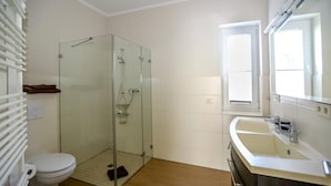 A bathroom with a glass-enclosed shower, a white toilet, a sink with a mirror, and a window. - Amselresidenz 4 - STAR (Binz)