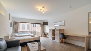 A modern hotel room with a bed, a desk, a chair, a sofa, and a television. - Room-value Stay Residence Mechelen - Stu (Mechelen)