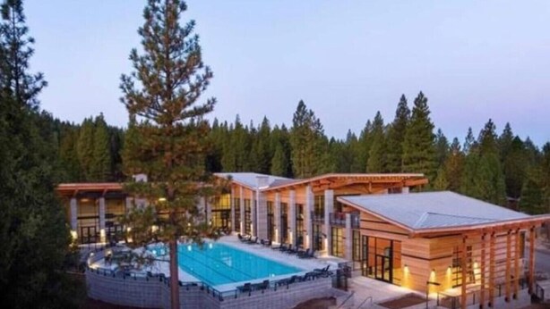 Un resort moderno con piscina, ventanas amplias y un bosque de fondo.