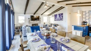 Un comedor amplio con una mesa larga dispuesta para una comida, una cocina con electrodomésticos modernos, y una sala de estar con chimenea y asientos cómodos.