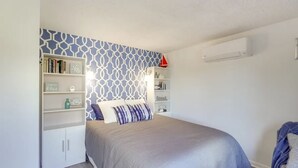 Un dormitorio con cama, una estantería y un aire acondicionado de pared.