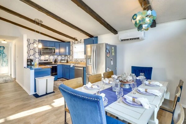 A modern kitchen with blue cabinets, a stainless steel refrigerator, and a dining area with a white table set for six.