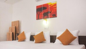 Hotelkamer met een bed, witte kussens, een bruin kussen, een wanddecoratie van een olifant en een boom, en een houten plank met handdoeken.