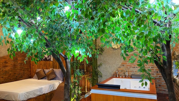 A bedroom with a bed, a wooden headboard, a large window, and a bathroom with a bathtub and a sink.