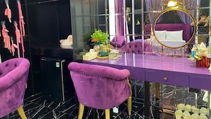 A purple vanity with a gold-framed mirror, a purple sofa, and a black trash bin.