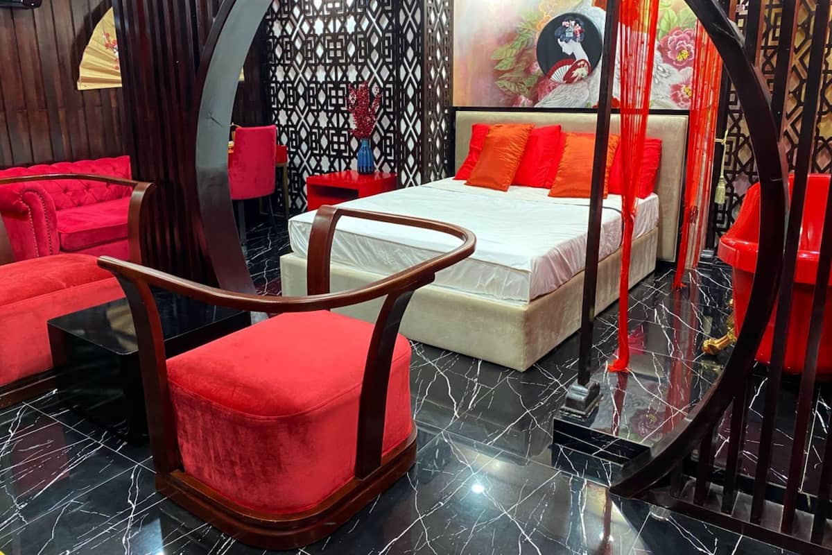 Une chambre d’hôtel moderne avec un grand lit, des fauteuils rouges à revêtement en tissu et un paravent noir décoratif.