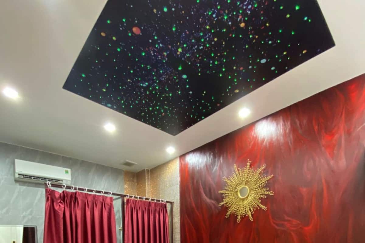 Une chambre à coucher avec un lit, un rideau rouge, un mur orné d’un motif solaire et un plafond étoilé.