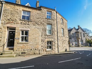 Un edificio de piedra con entrada en esquina, una ventana visible y un cartel que dice 'Corner Cottage'.