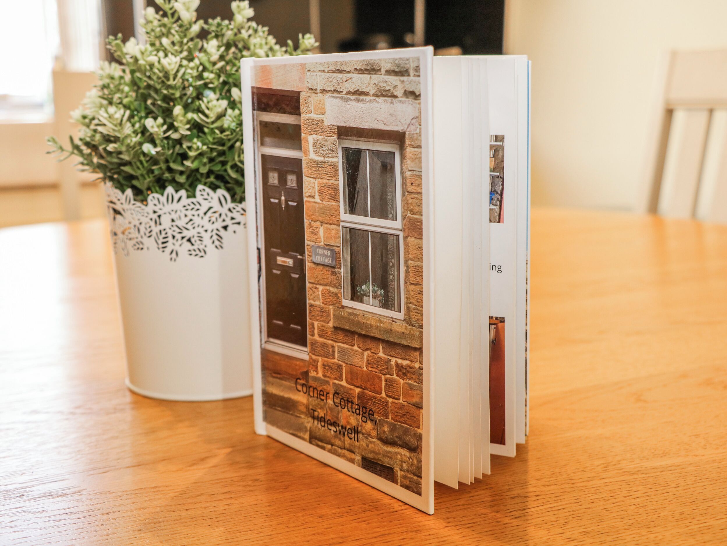 Un livre dont la couverture représente un mur de briques, intitulé « Corner Cottage Tideswell », est posé sur une table en bois.
