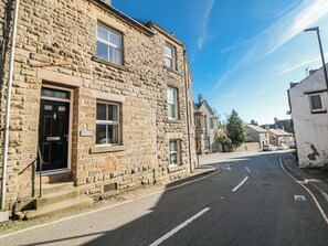A stone building with a black door, a window with a sign, and a clear sky. - Corner Cottage (Buxton)