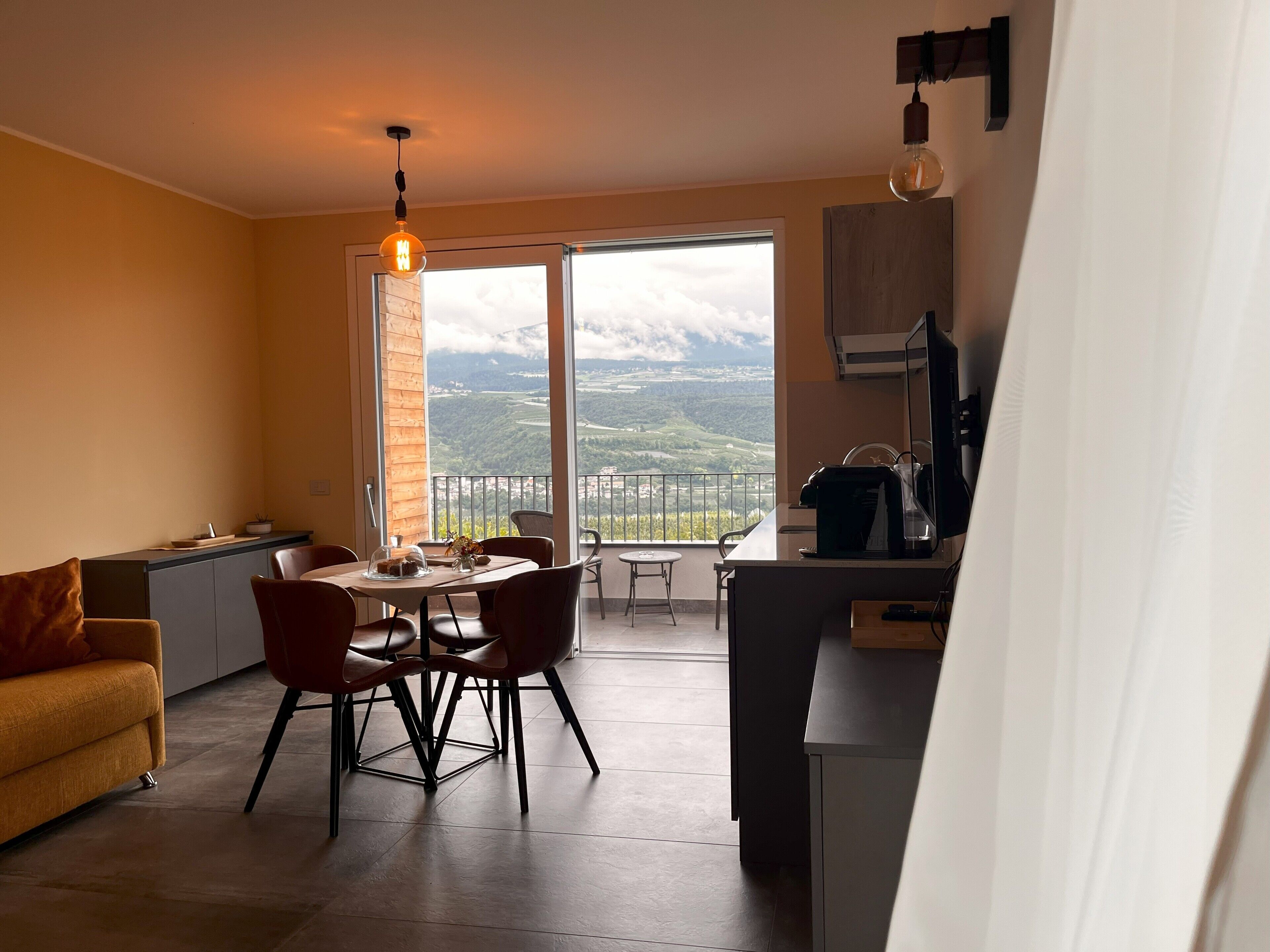 A modern kitchen with a dining area, a sofa, and a view of the countryside.