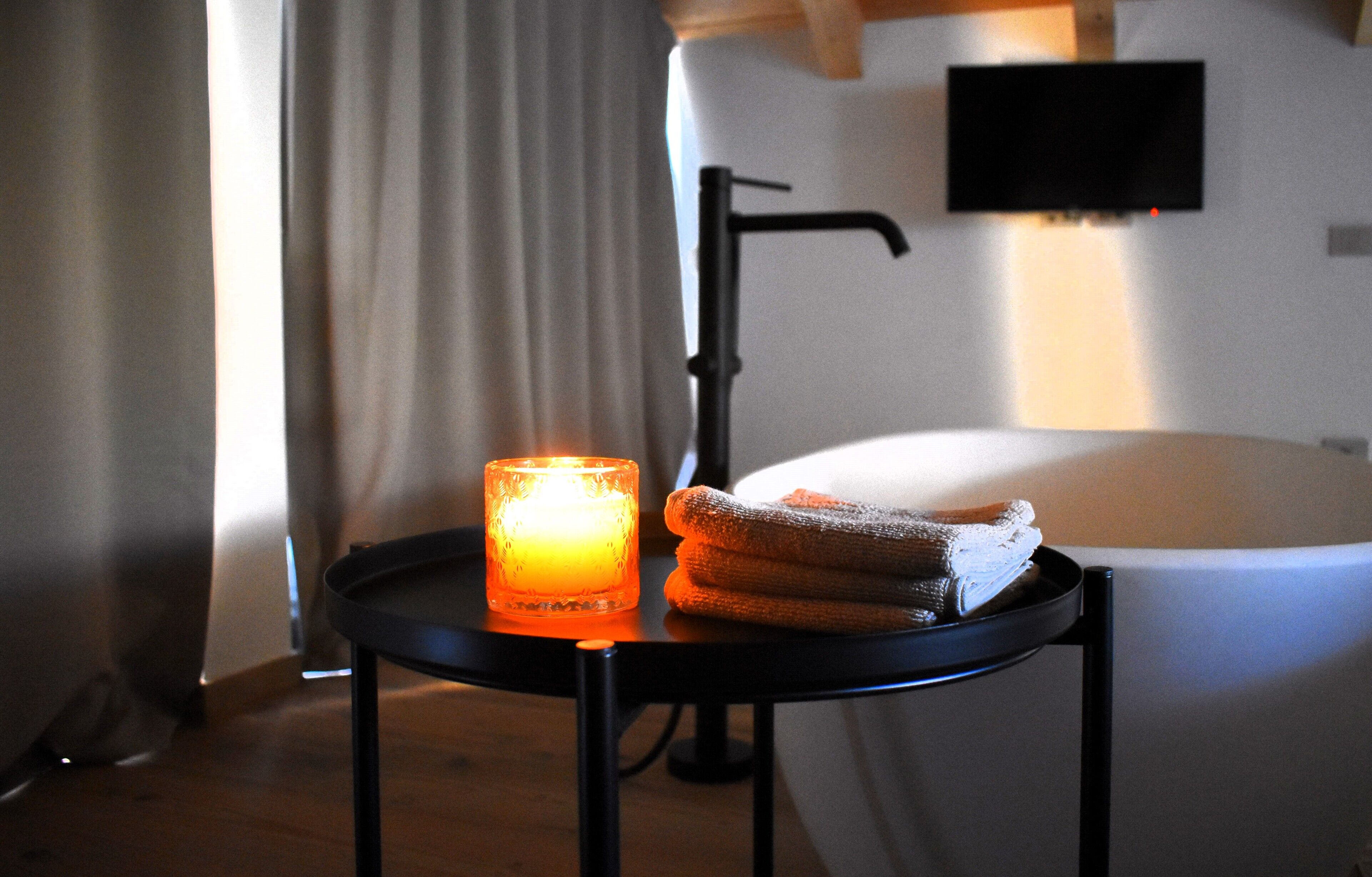 A bathroom with a bathtub, a candle, and towels on a small table.