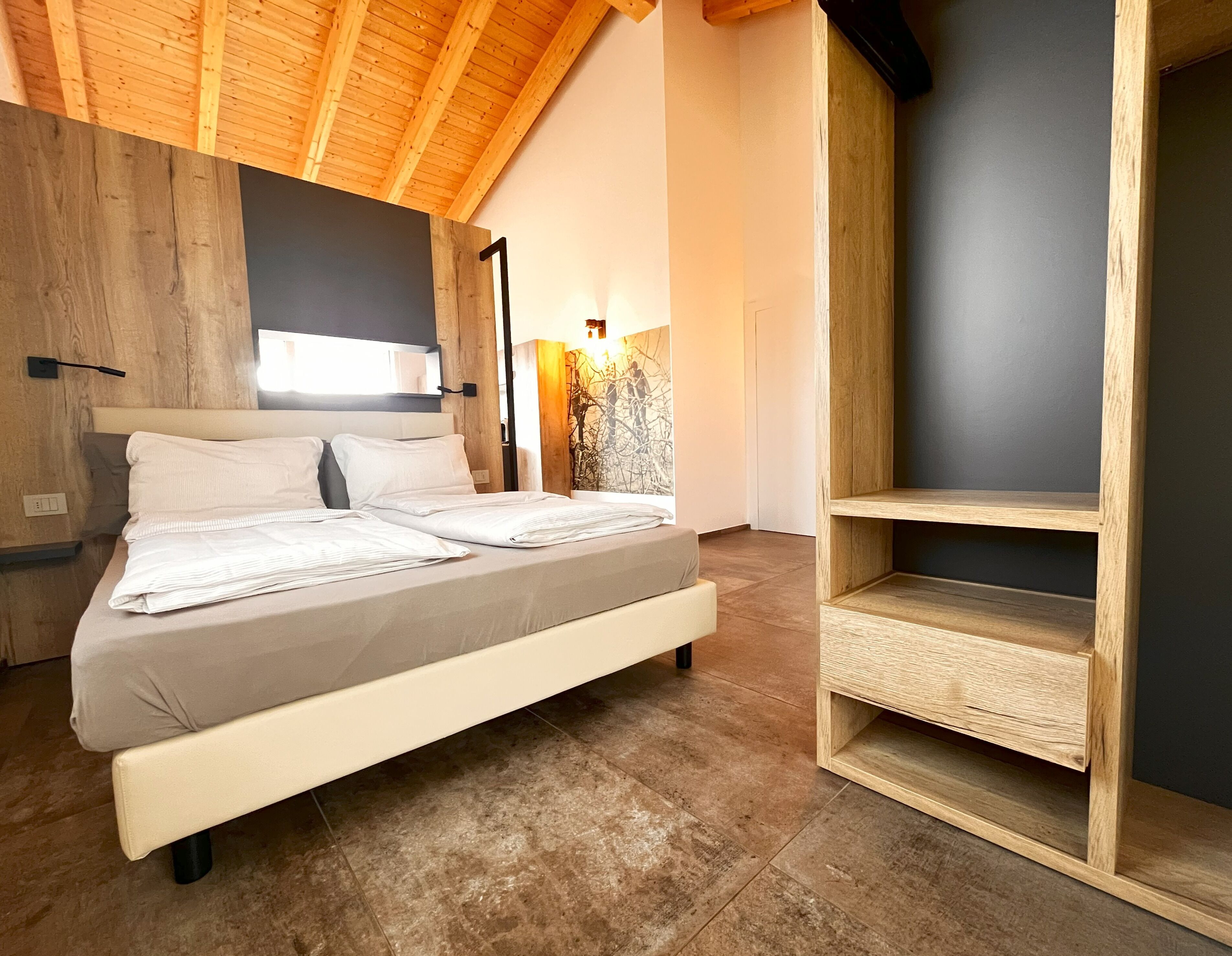 Un dormitorio moderno con techo de madera, una cama con ropa blanca, un armario de madera y una estantería de pared.