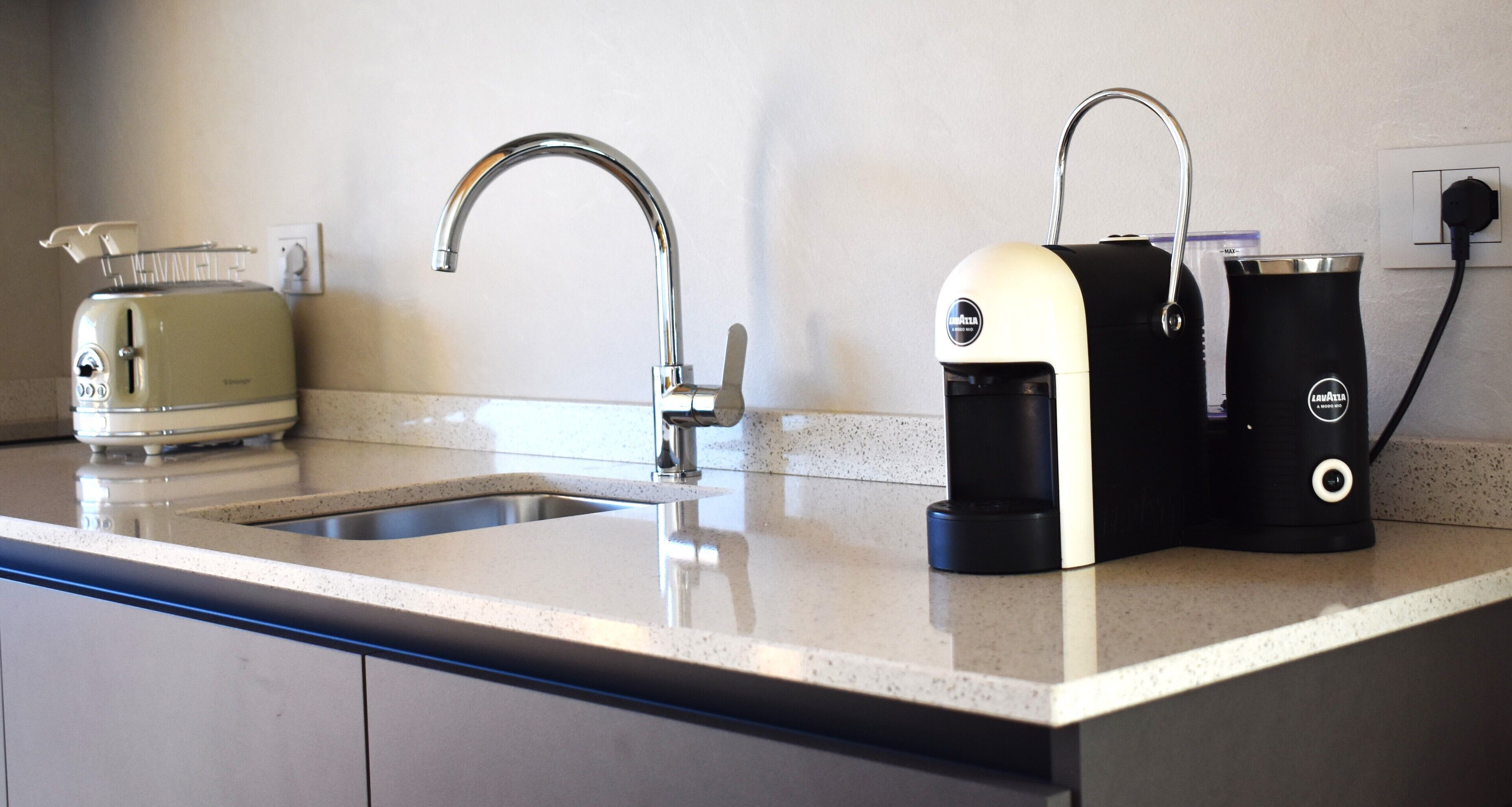 Une cuisine au design moderne, comprenant un évier en acier inoxydable, un grille-pain et une machine à café.