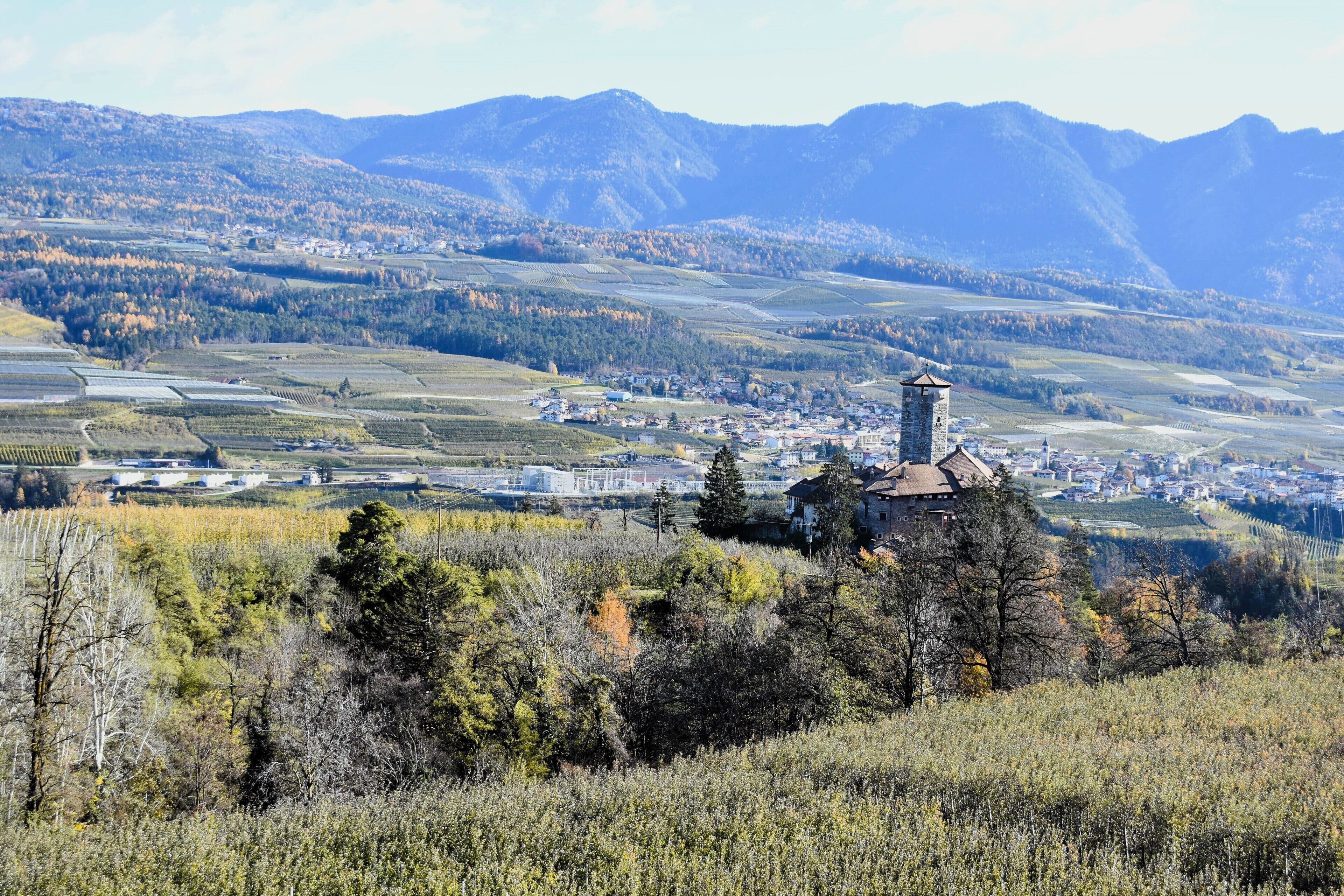 A town with a prominent tower, surrounded by mountains and fields.