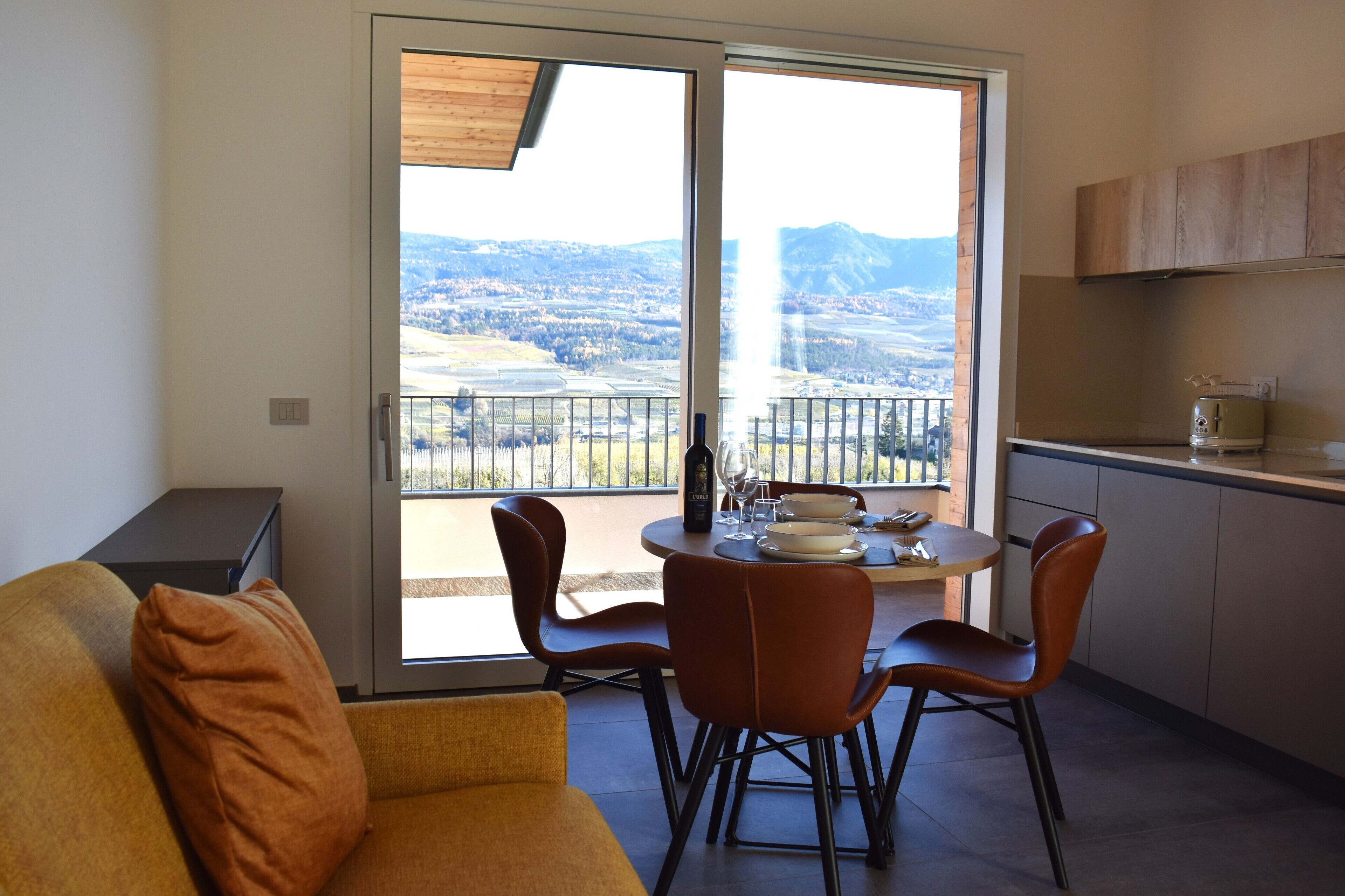 Un'area pranzo con un tavolo apparecchiato per due, un divano e una zona cucina con pensili e un piano di lavoro.