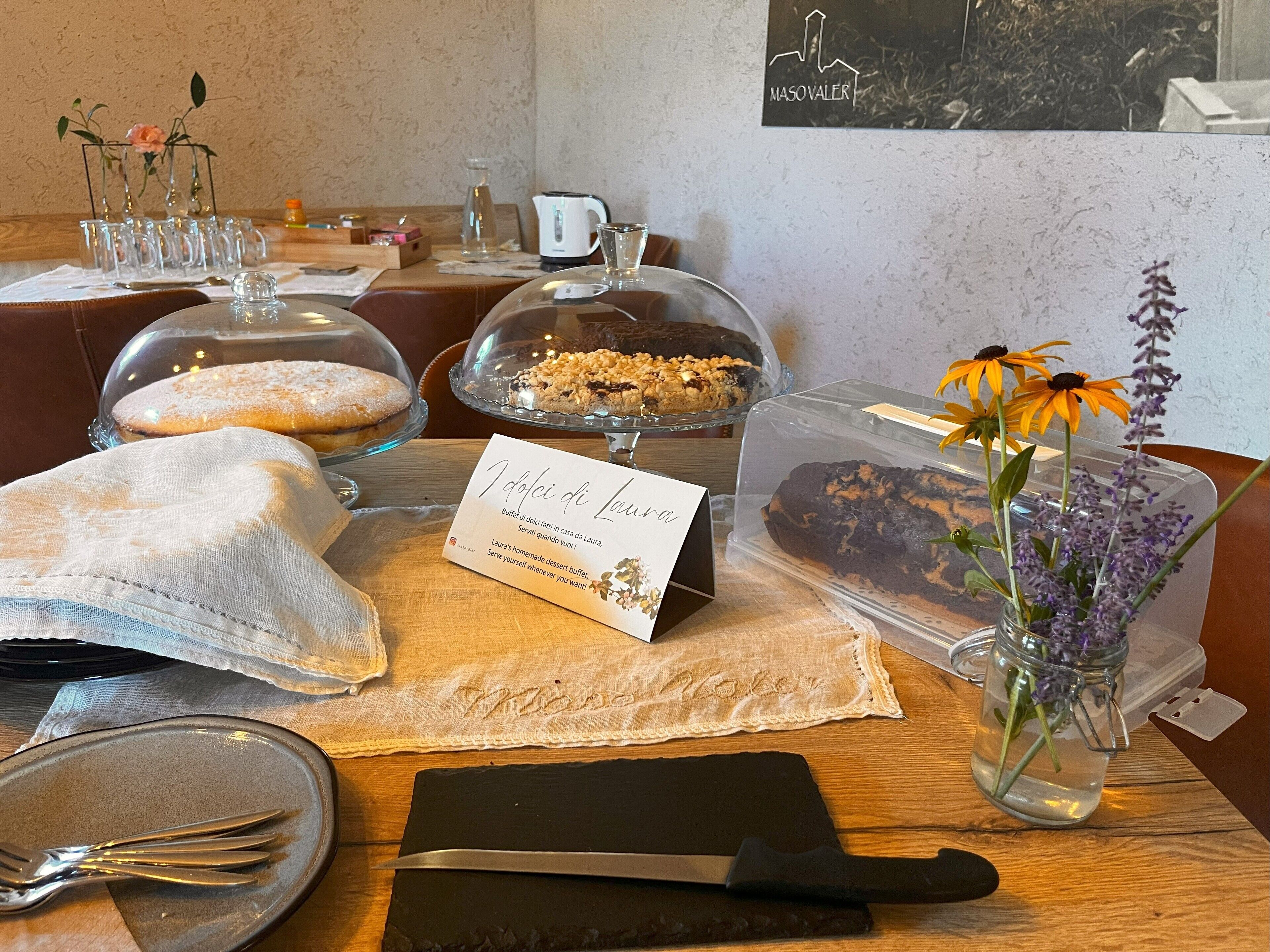 A buffet table with various desserts, a sign for Laura's homemade desserts, and a vase with flowers.