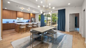 A modern kitchen with wooden cabinets, a central island, and a dining area with a large table and chairs. - Contemporary Remodeled Bungalow - Pet Friendly! (San Antonio)