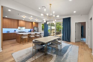 A modern kitchen with wooden cabinets, a central island, and a dining area with a large table and chairs. - Contemporary Remodeled Bungalow - Pet Friendly! (San Antonio)