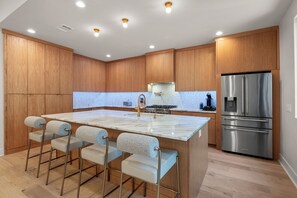 A modern kitchen with wooden cabinets, a marble island with bar stools, a stainless steel refrigerator, and a gas stove. - Contemporary Remodeled Bungalow - Pet Friendly! (San Antonio)