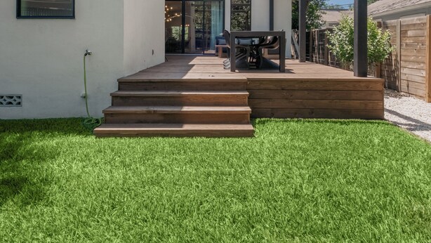 Una casa moderna con un porche cubierto, una terraza de madera y un césped bien cuidado.