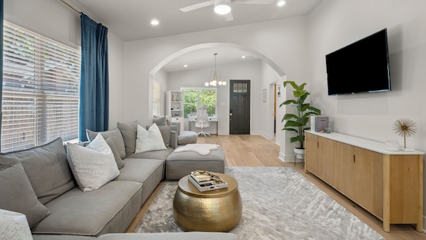 A modern living room with a sectional sofa, a round gold coffee table, and a flat-screen TV mounted on the wall. - Contemporary Remodeled Bungalow - Pet Friendly! (San Antonio)