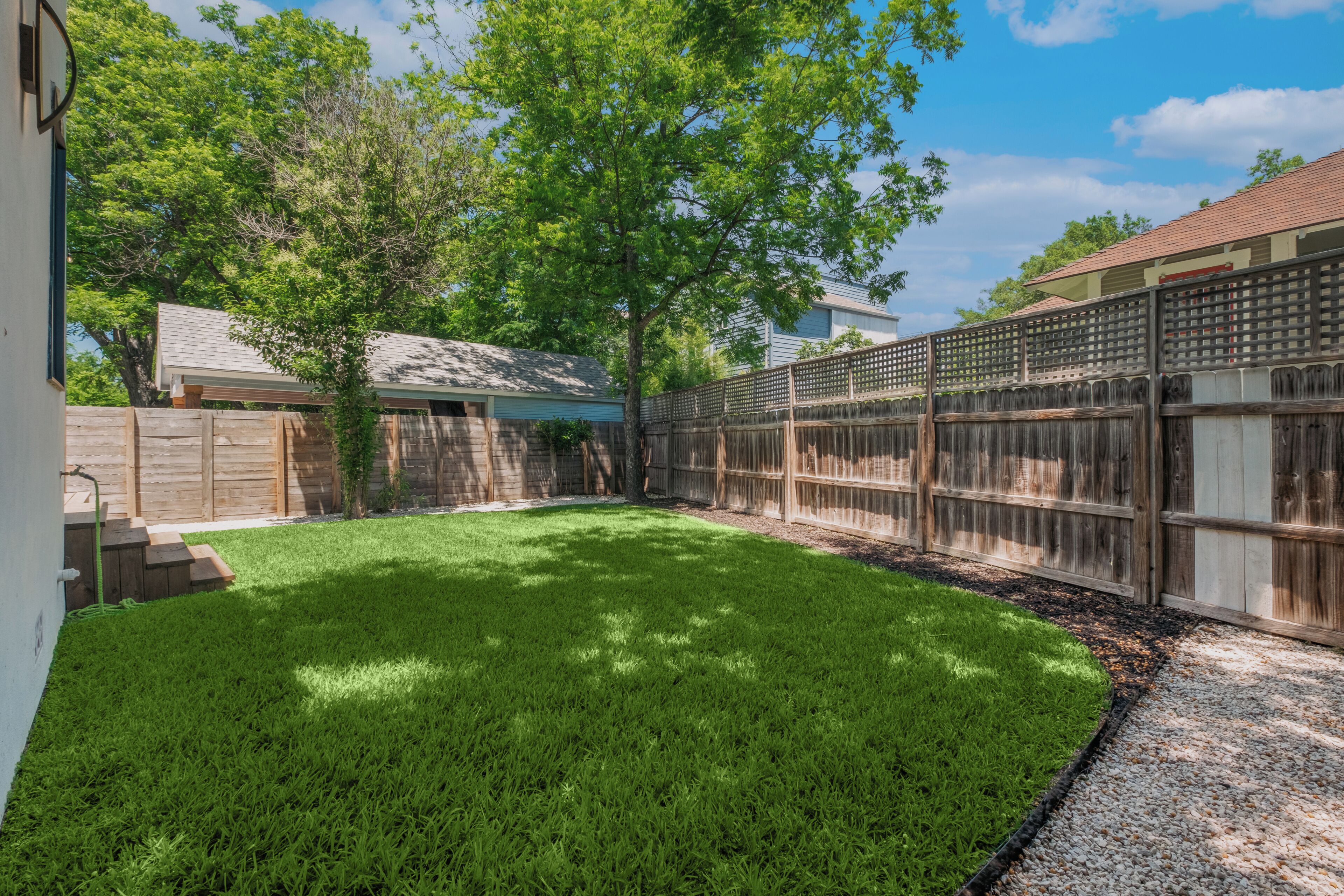A backyard with a well-maintained lawn, a wooden fence, and a tree.