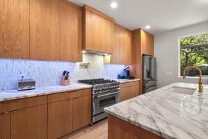 A modern kitchen with wooden cabinets, a gas stove, a stainless steel refrigerator, and a marble countertop. - Contemporary Remodeled Bungalow - Pet Friendly! (San Antonio)