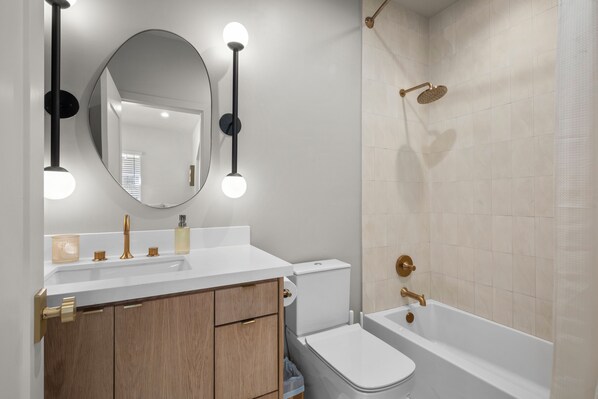 A bathroom with a white sink, a mirror, a toilet, and a bathtub. - Contemporary Remodeled Bungalow - Pet Friendly! (San Antonio)