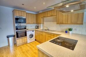 Una cocina moderna con armarios de madera, electrodomésticos de acero inoxidable, lavadora y encimera de granito.