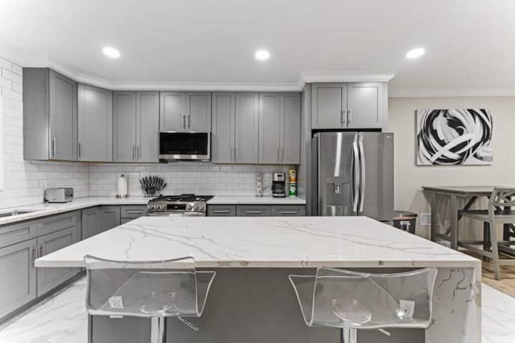 Una cucina moderna con mobili grigi, un'isola grande, elettrodomestici in acciaio inossidabile e una TV a schermo piatto.