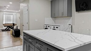 A modern kitchen with marble countertops, grey cabinets, and a built-in washing machine. - Fun, Stylish, Pool table, Darts (Camden)