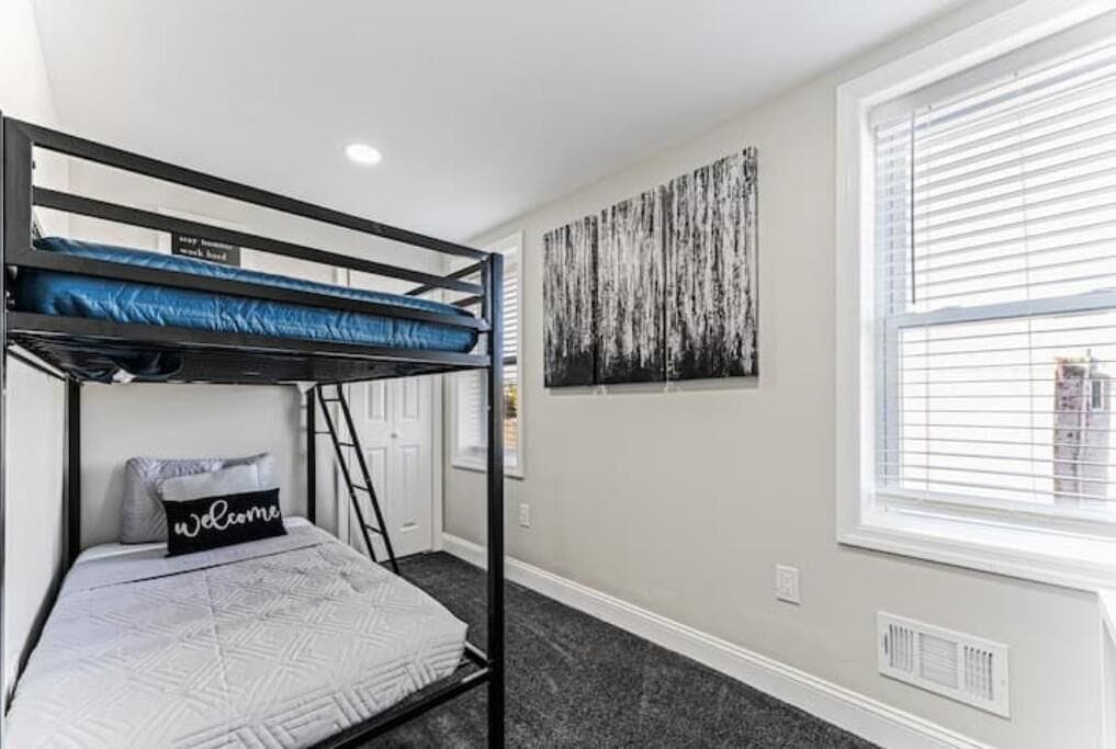 Habitación con literas, una almohada de bienvenida, una escalera, una ventana con persianas y un cuadro colgado en la pared.