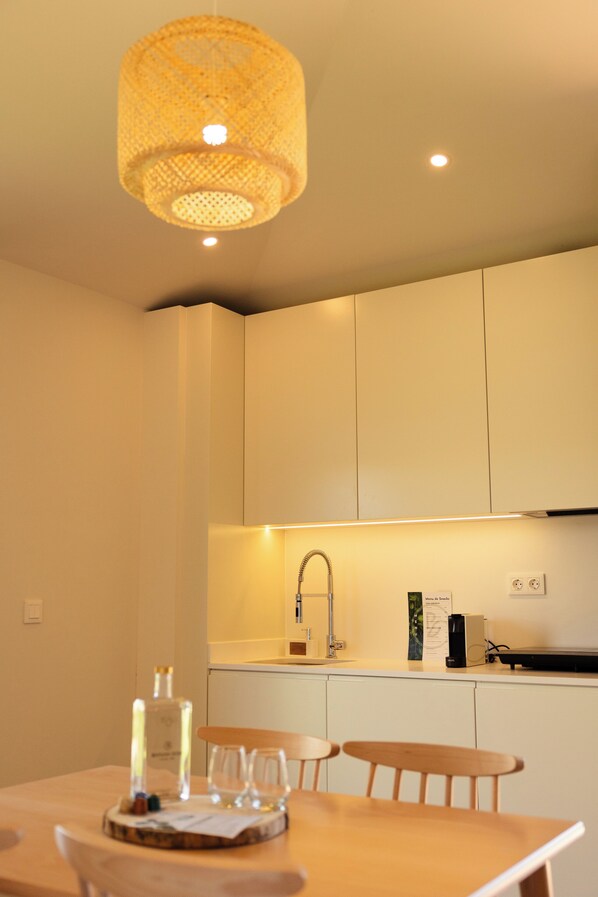 A modern kitchen with white cabinets, a hanging light fixture, and a dining area with a wooden table and chairs. - Batalha Golf Villas & Spa (Ponta Delgada)