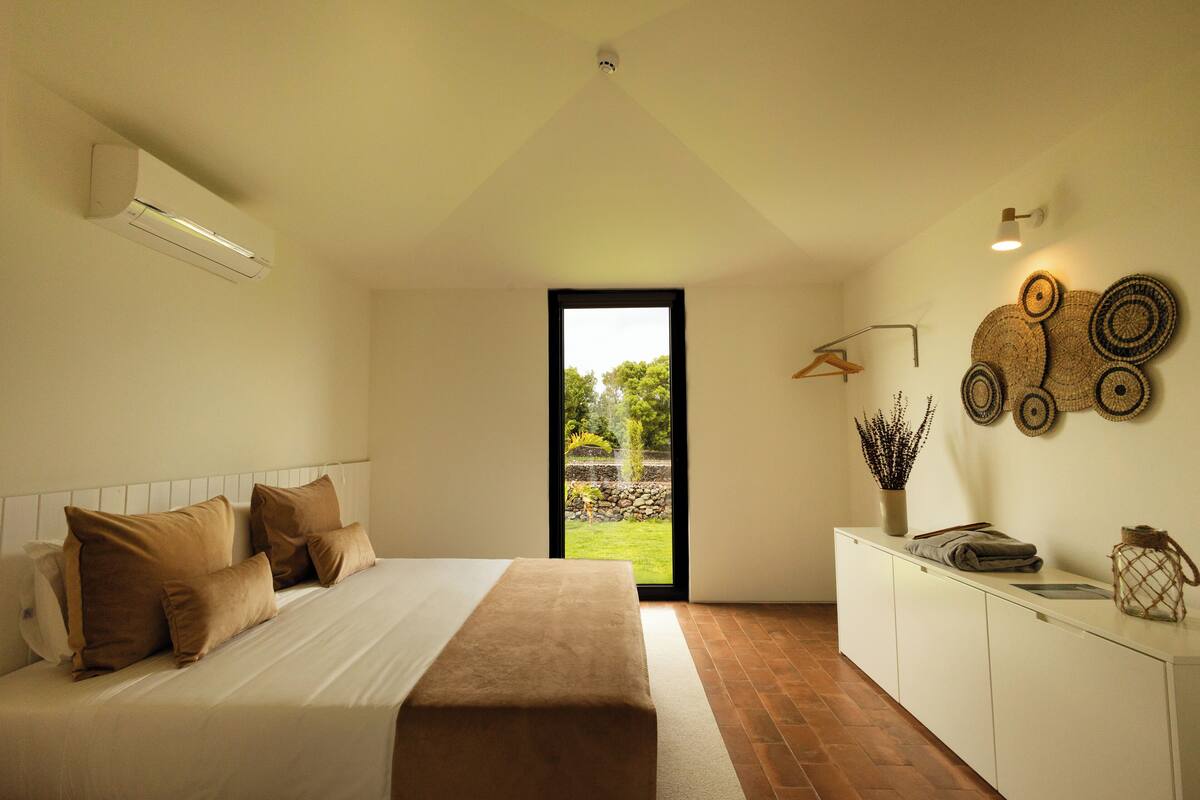 A bedroom with a bed, a bedside table, a window, and a view of the outdoors.