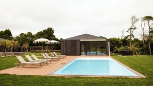 A modern outdoor pool area with lounge chairs and umbrellas, surrounded by greenery. - Batalha Golf Villas & Spa (Ponta Delgada)