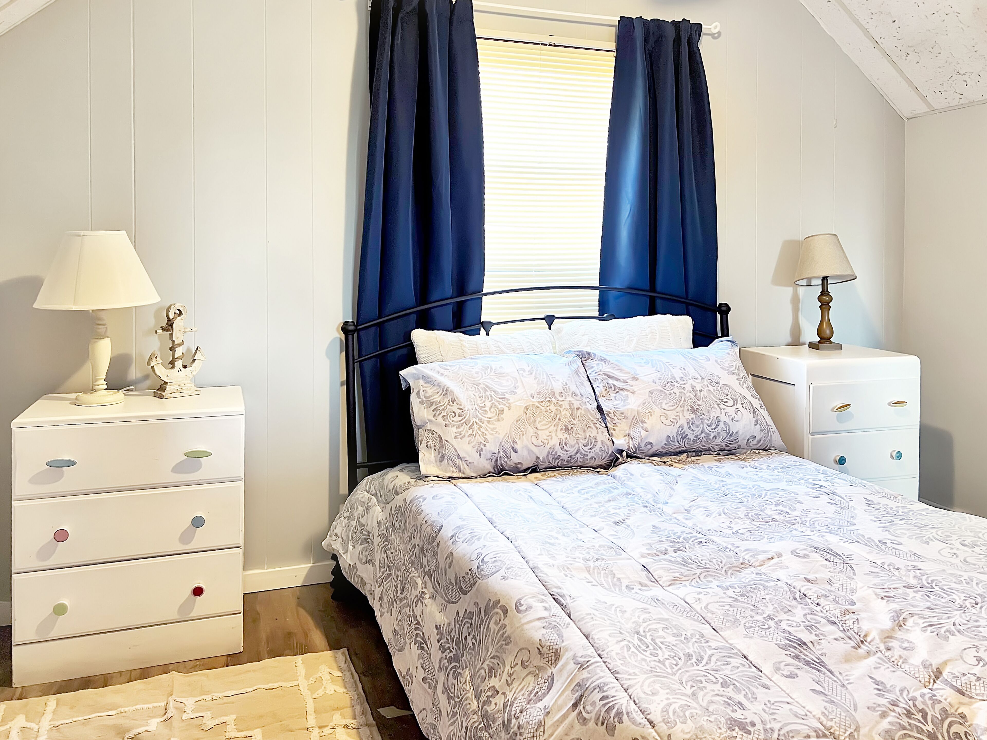 Een slaapkamer met een bed, twee nachtkastjes, een wandlamp en een raam met gordijnen.