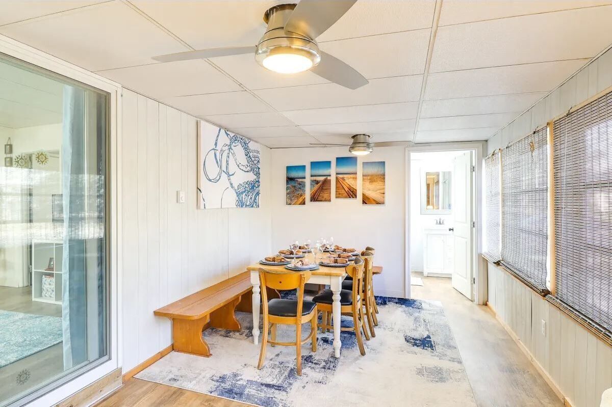 Comedor con mesa dispuesta para seis personas, ventilador de techo y vista hacia otra habitación.