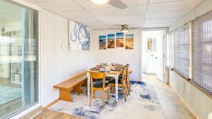 Un coin repas avec une table dressée pour six personnes, un ventilateur de plafond et une vue sur une autre pièce.