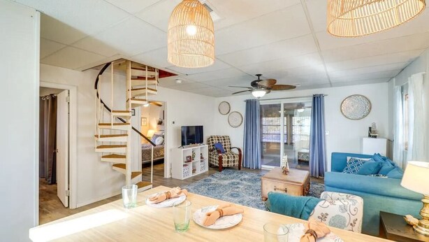 Un vaste espace de vie agrémenté d’un escalier en bois, d’une table à manger dressée avec des assiettes et des verres, d’un canapé bleu et d’un ventilateur de plafond.